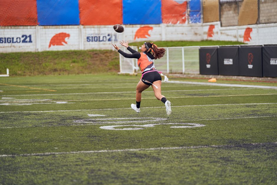 Young female athlete in action catching a football on a sports field.