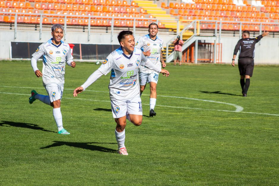 Soccer players in white jerseys celebrating a goal on the field during a daytime match.