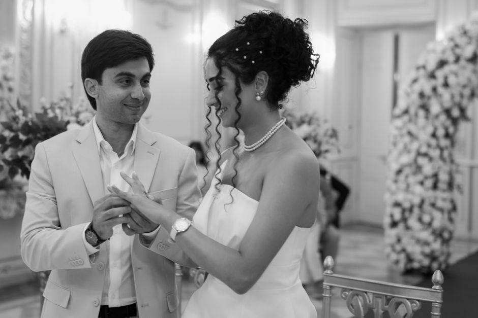 A couple exchanging rings during an elegant indoor wedding ceremony, captured in black and white.