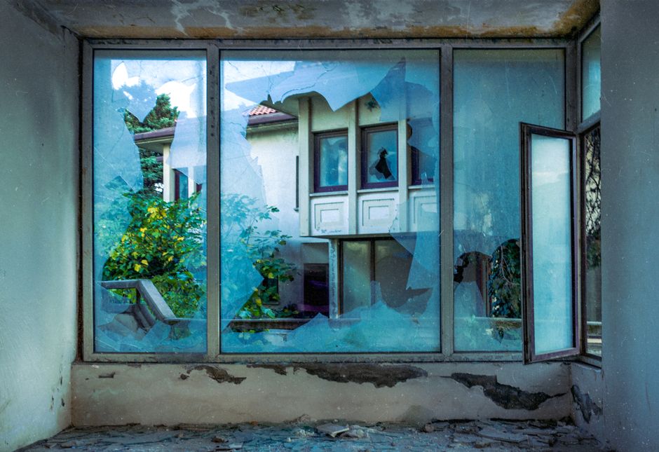 View through broken window of an empty house, showcasing decay and nature.