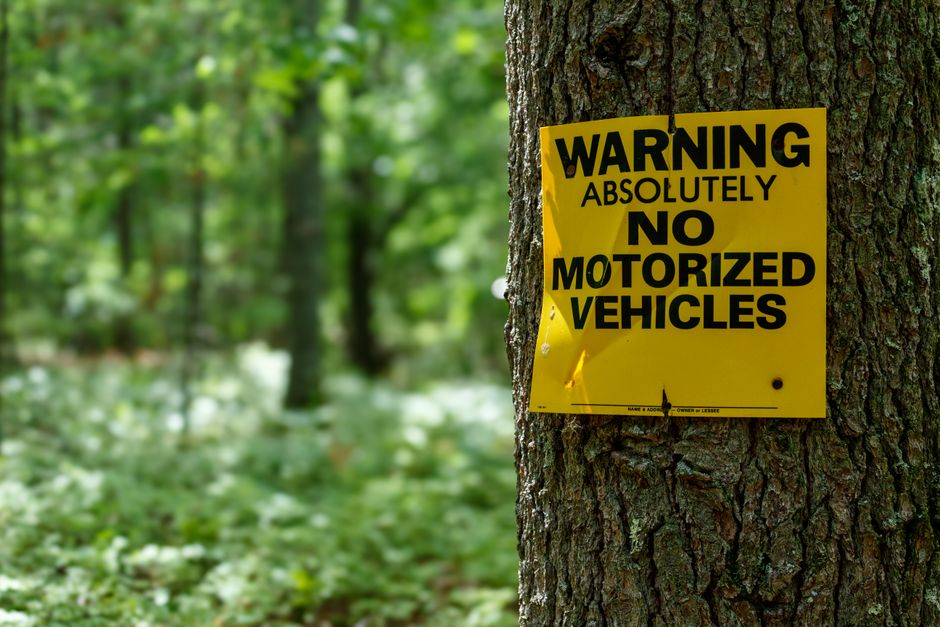 Yellow warning sign on a tree in a lush forest, prohibiting motorized vehicles.