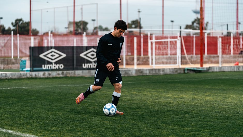 A player in black sportswear dribbles a soccer ball on a field.