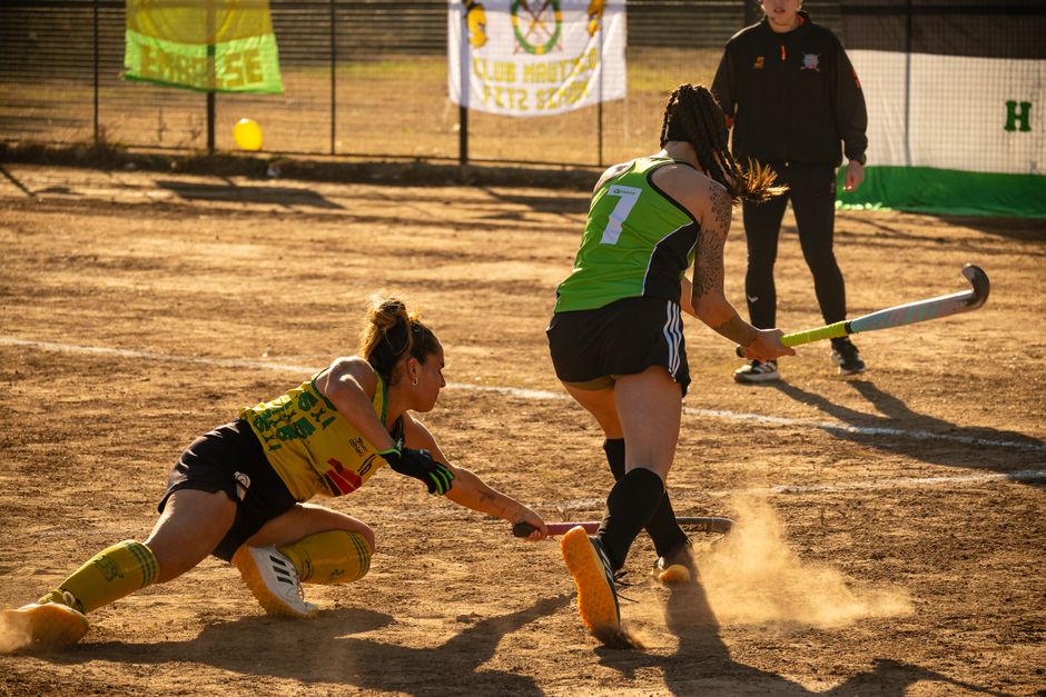 Action-packed field hockey match captured on a dusty outdoor field during the day.