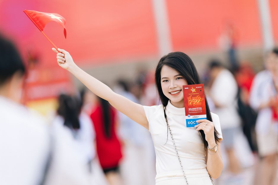 Smiling woman in white dress waving a red flag at a vibrant outdoor event.