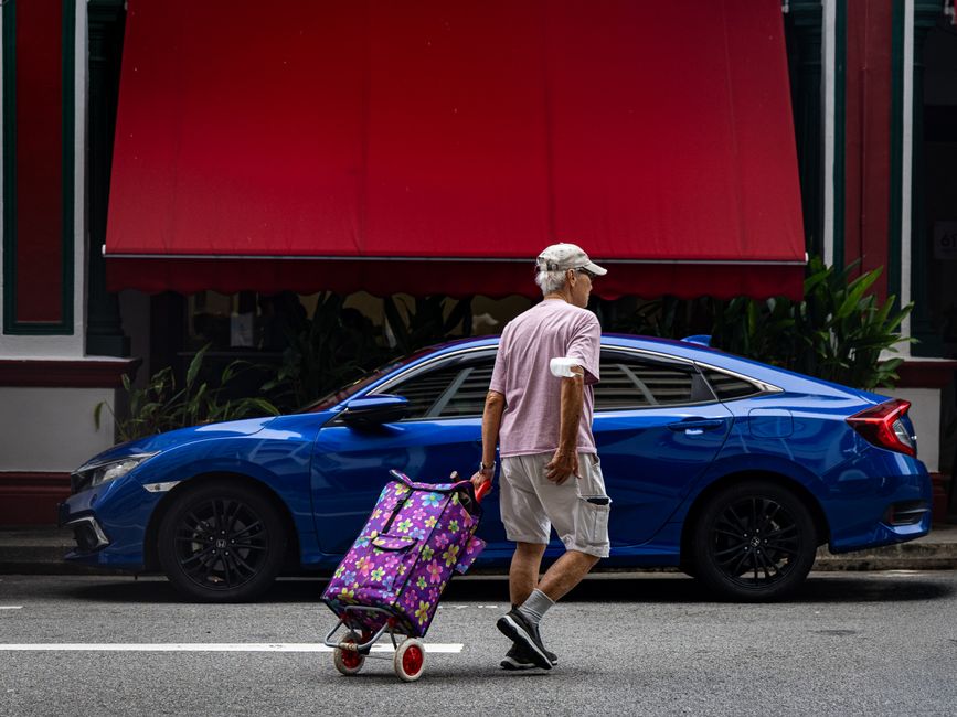 Senior man pulling floral shopping cart across street in urban setting.