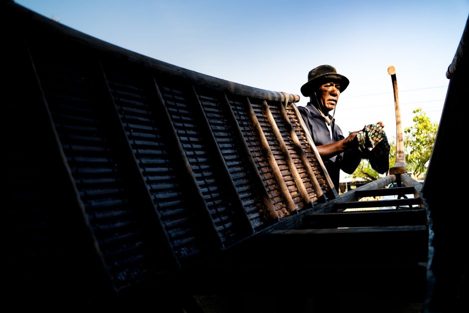 An African fisherman repairs a wooden boat under a clear blue sky, capturing traditional craftsmanship.