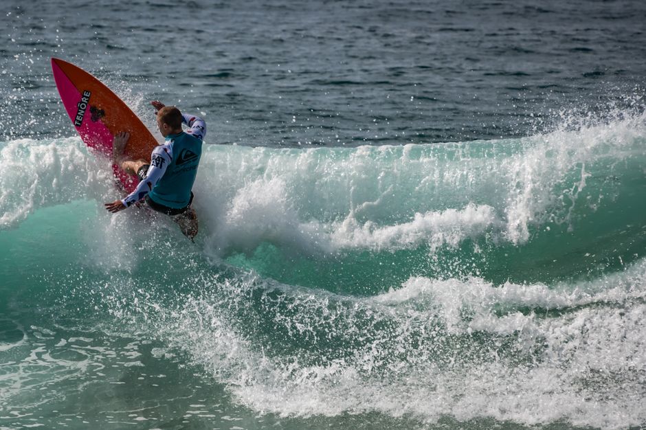 A surfer performs an impressive maneuver on a crashing ocean wave, showcasing thrilling water sports action.