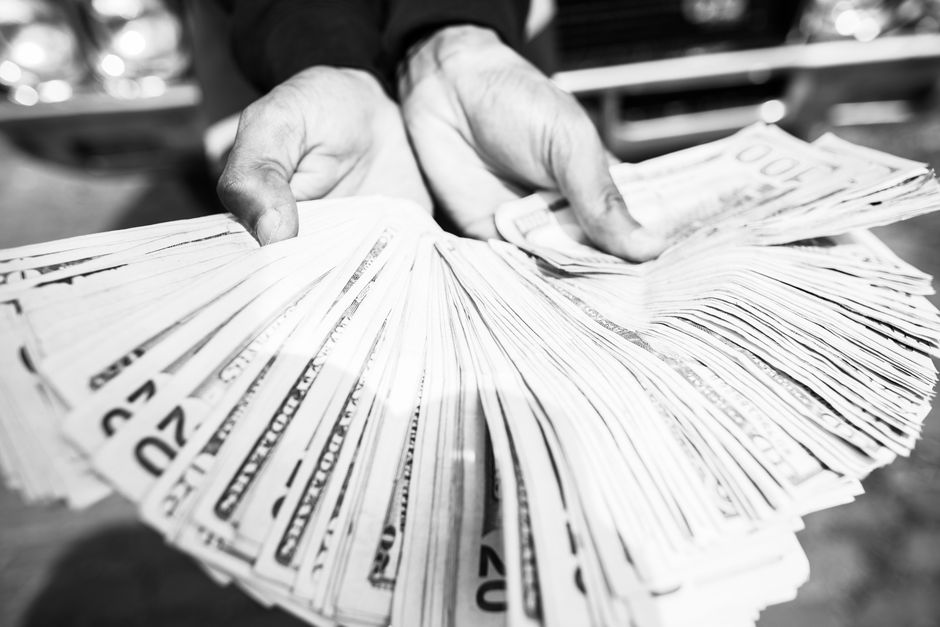 Close-up of hands holding a large amount of cash in black and white.