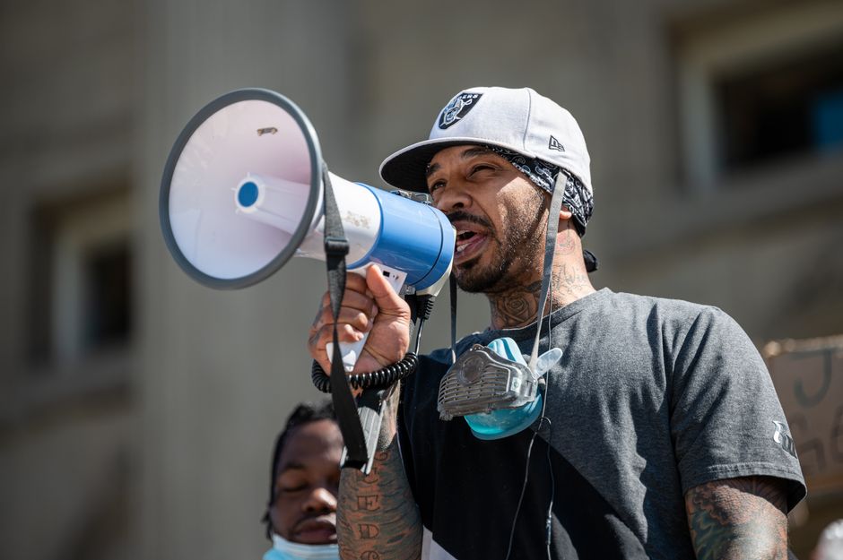 Low angle of African American man with tattoos in casual clothes and cap standing on protest and talking on loudspeaker during coronavirus
