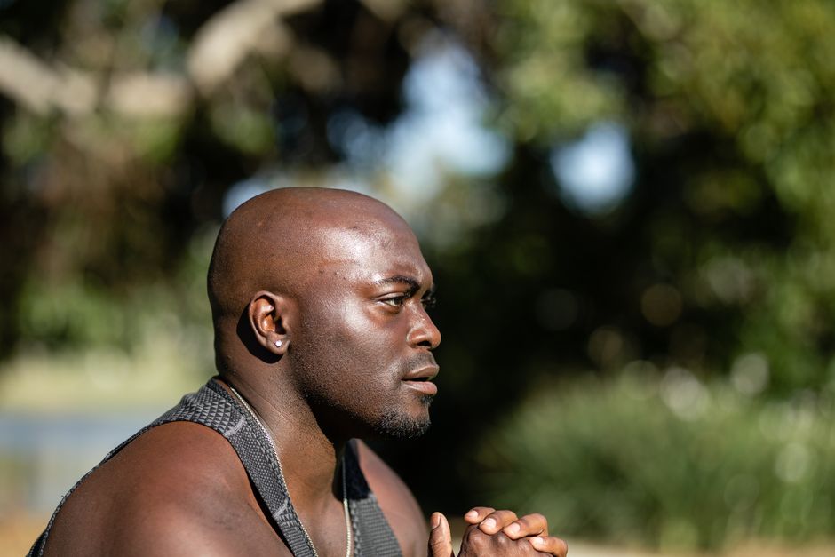 Close-up of a bald African American man outdoors in nature, looking thoughtful.