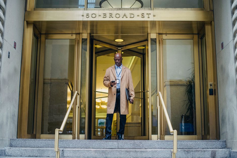 From below of attentive African American male in elegant outfit checking mobile phone near entrance of business center
