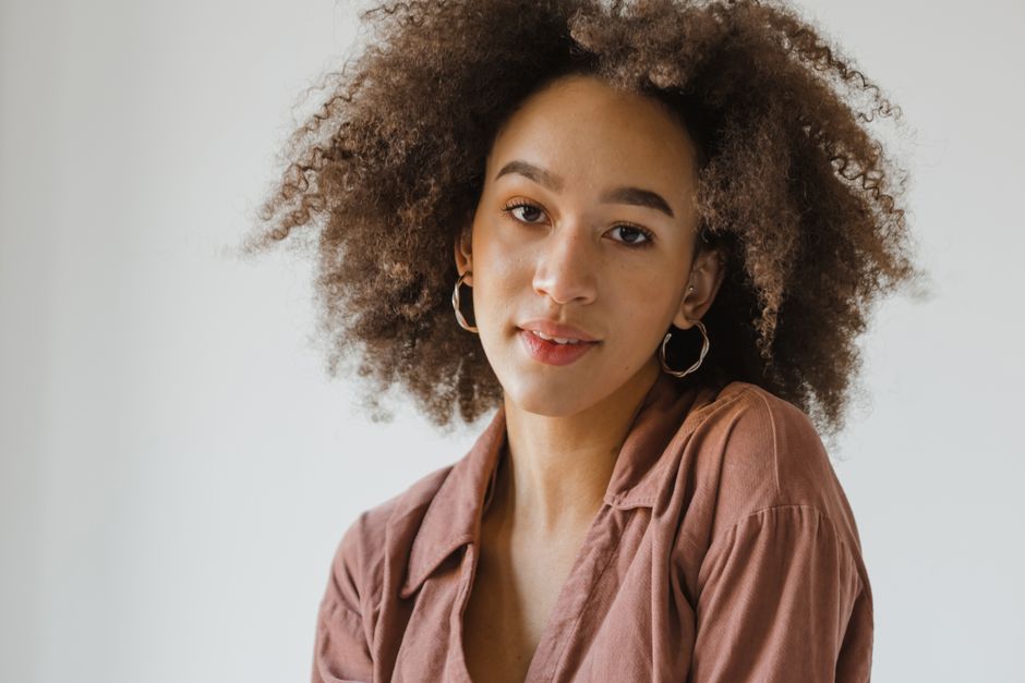 Beautiful studio portrait of a woman with natural curly hair and hoop earrings, exuding confidence and style.