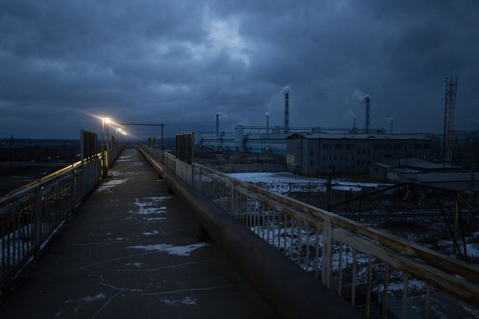 Long bridge with bright luminous streetlamps across railway tracks under gloomy cloudy sky in dusk