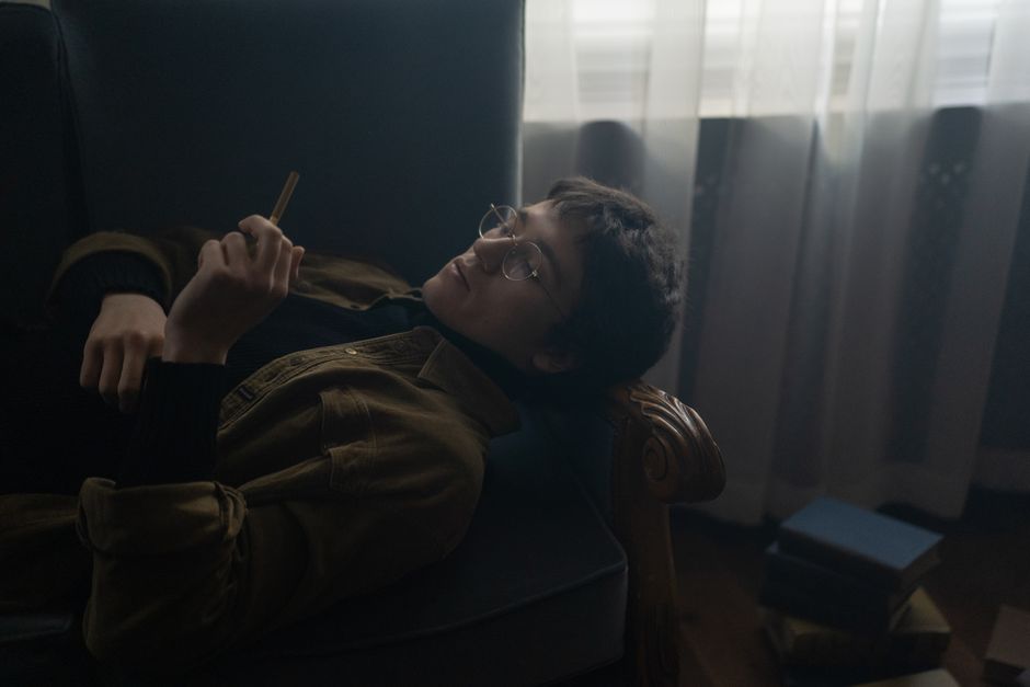 Young woman with short hair relaxing on sofa indoors, holding a cigarette.