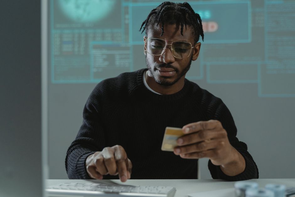 Man with glasses holding a bank card while typing on a keyboard, sitting in front of a computer.