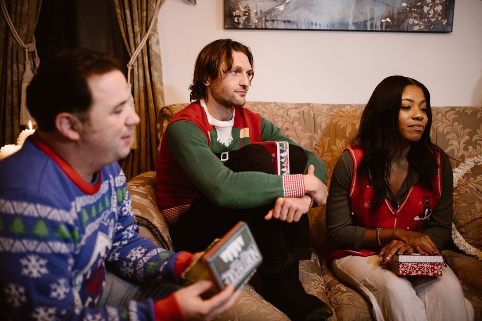 Happy family celebrating Christmas with gifts on a cozy sofa, wearing festive sweaters indoors.