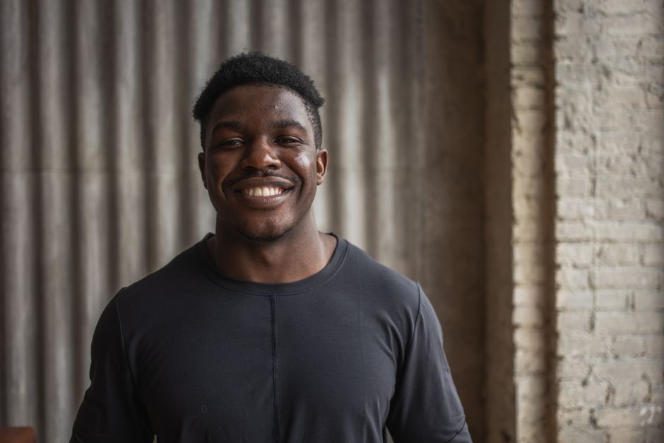 Content adult black male athlete looking at camera with toothy smile against ribbed wall