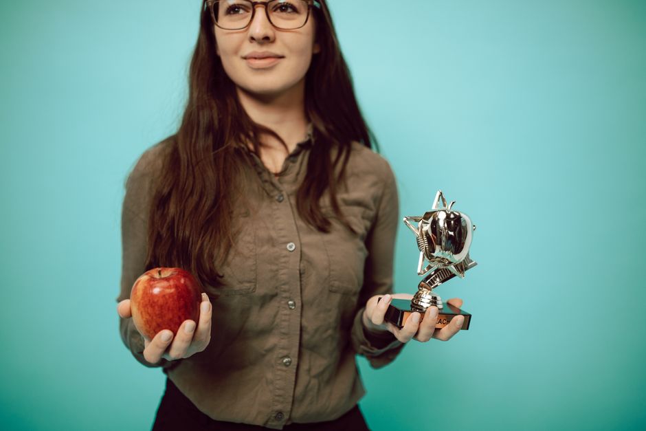 Woman holding an award trophy and apple against a turquoise background, symbolizing achievement and balance.