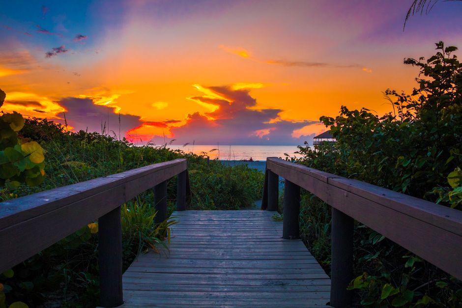 Peaceful sunset view over a wooden boardwalk leading to the ocean in Avon Park, FL.