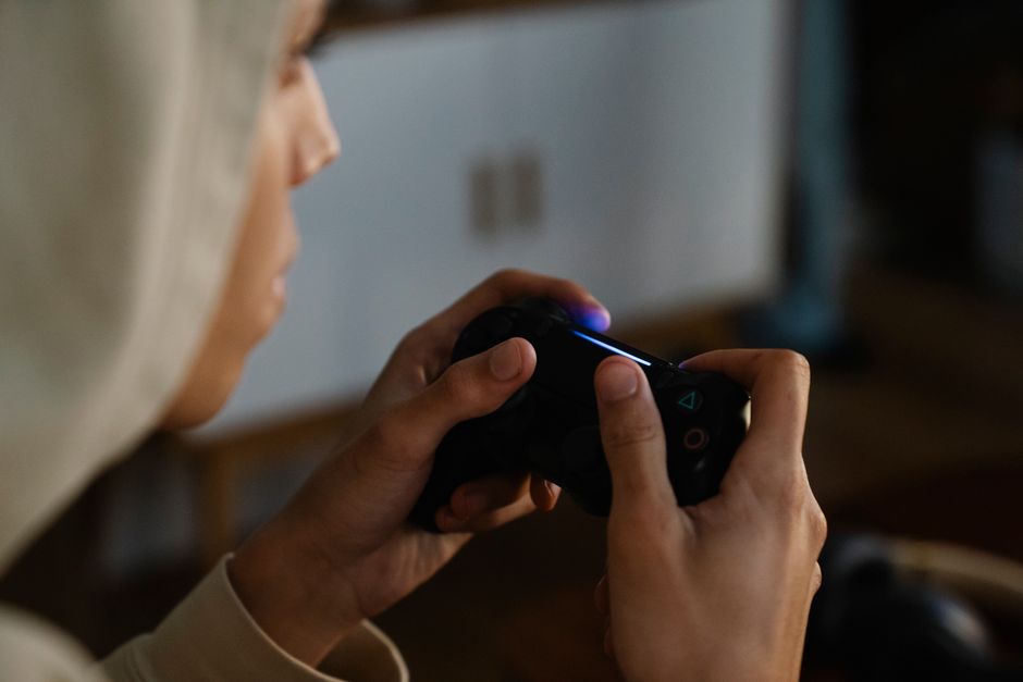 Side view of crop young ethnic male gamer with console controller playing video game in room