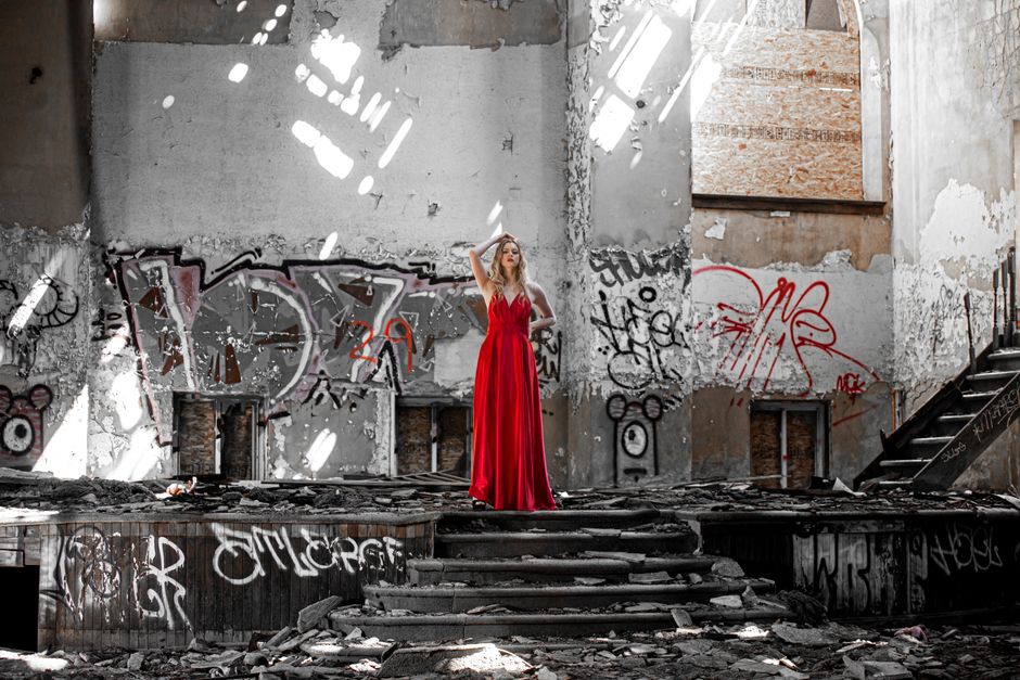 Elegant woman in a red dress poses in an abandoned, graffiti-covered building.