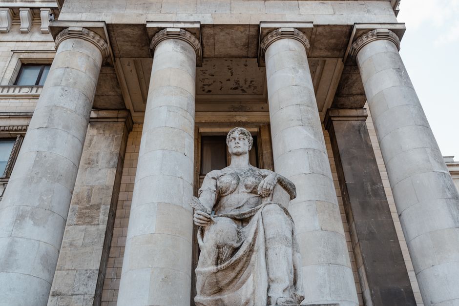 Majestic neoclassical building facade with statue and pillars, photographed in daylight.