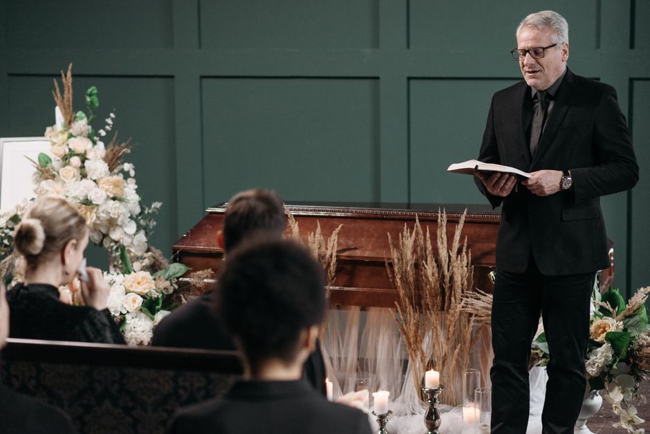 Pastor leading a funeral service with a coffin and floral arrangements.