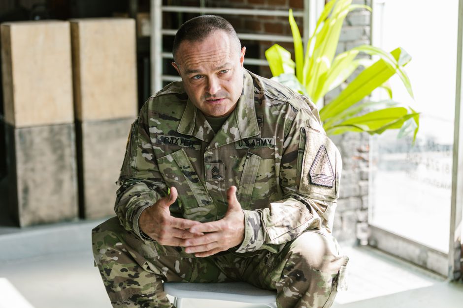US Army soldier in a military uniform sitting indoors, discussing mental health support.