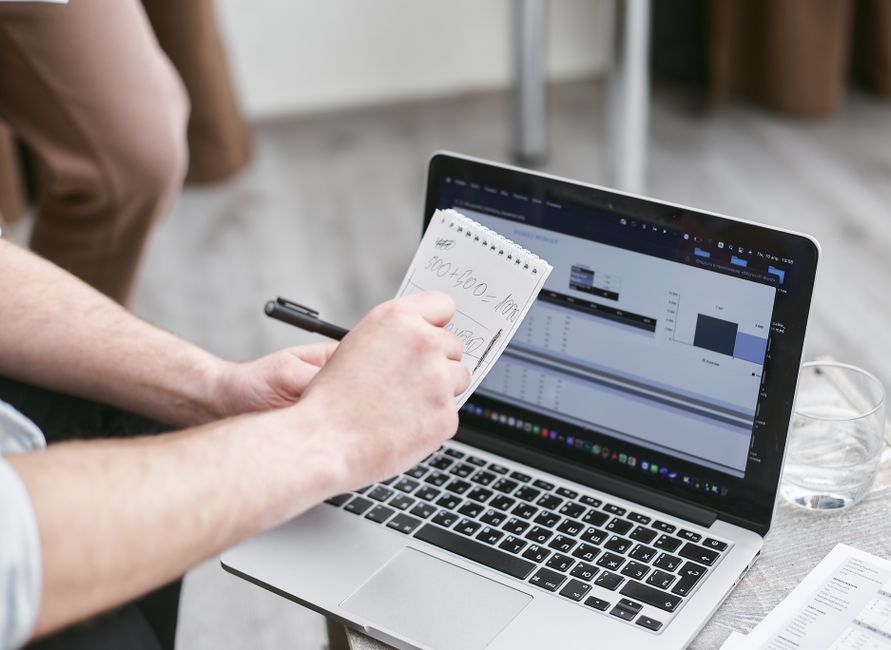 Person analyzing data on laptop while taking notes, focusing on market trends.