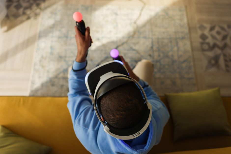 A person wearing virtual reality glasses and using controllers, viewed from above, indoors.