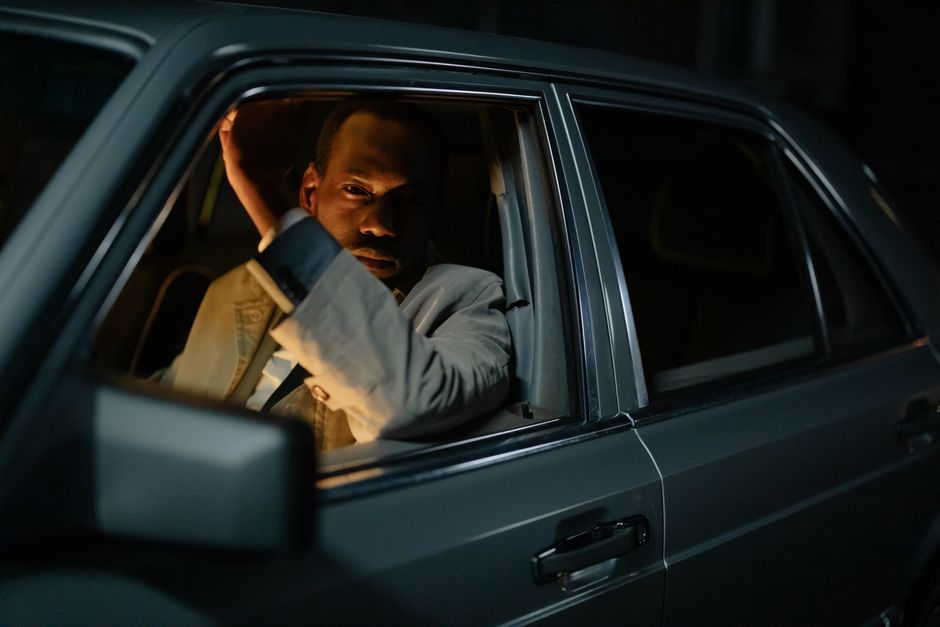 A contemplative African American man peers out of a car window during nighttime.