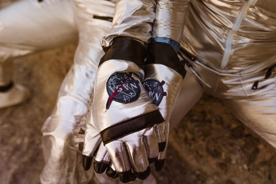 A close-up of two astronauts wearing silver space suits, holding hands, reflecting sci-fi themes.