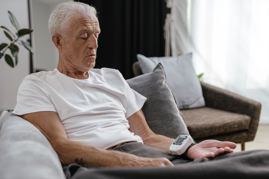 Elderly man measuring blood pressure with digital device while relaxing at home.