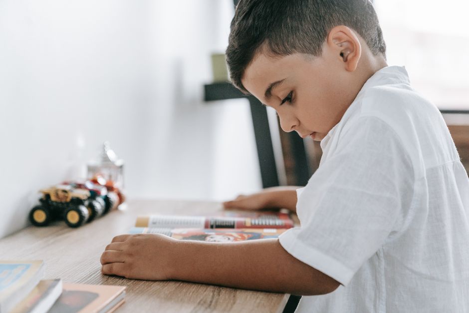 A young boy engages in reading at a desk indoors, showcasing childhood curiosity.